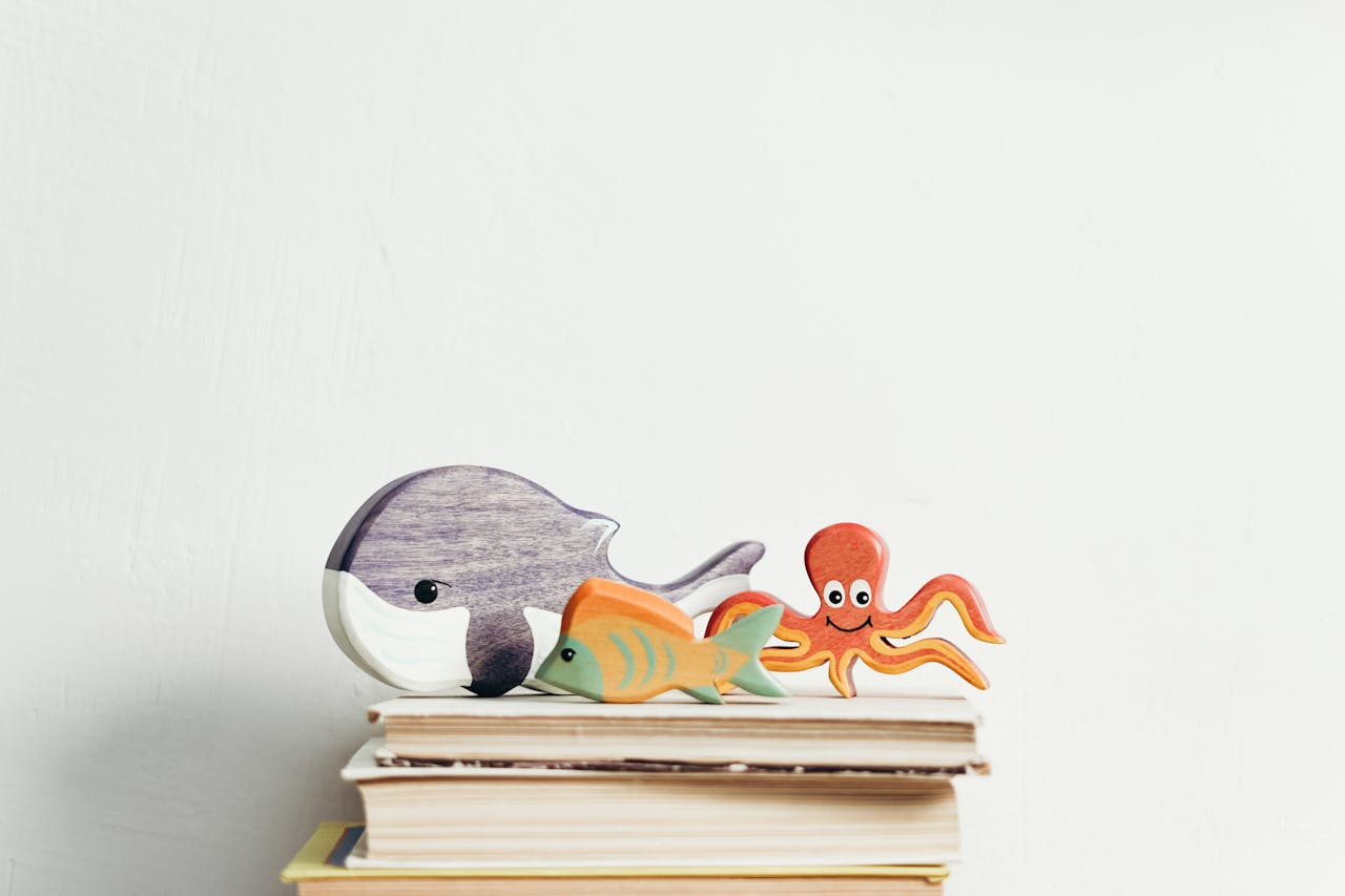 Charming wooden toys of marine animals on stacked books with a white background, perfect for kids' decor.