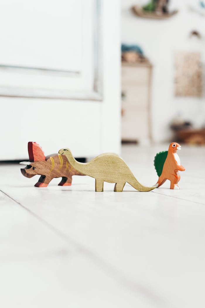 A lineup of colorful wooden dinosaur toys on a light wooden floor in a playroom.