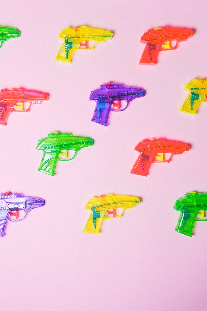 Colorful toy water guns on a pink background arranged in a pattern.