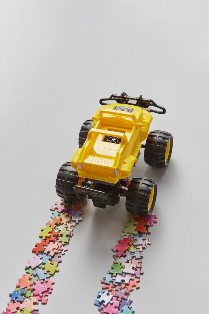 Yellow toy truck driving over colorful puzzle pieces creating a unique pattern.