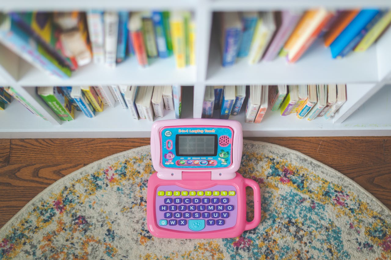 Colorful children's toy laptop on a rug beside a bookshelf with colorful books.
